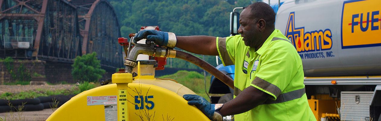 Adams Petroleum employee retrieving fuel at a gas pump in front of a bridge.