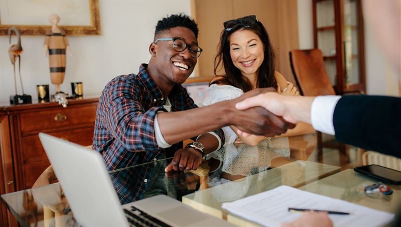 young couple smile shaking hands with a banker