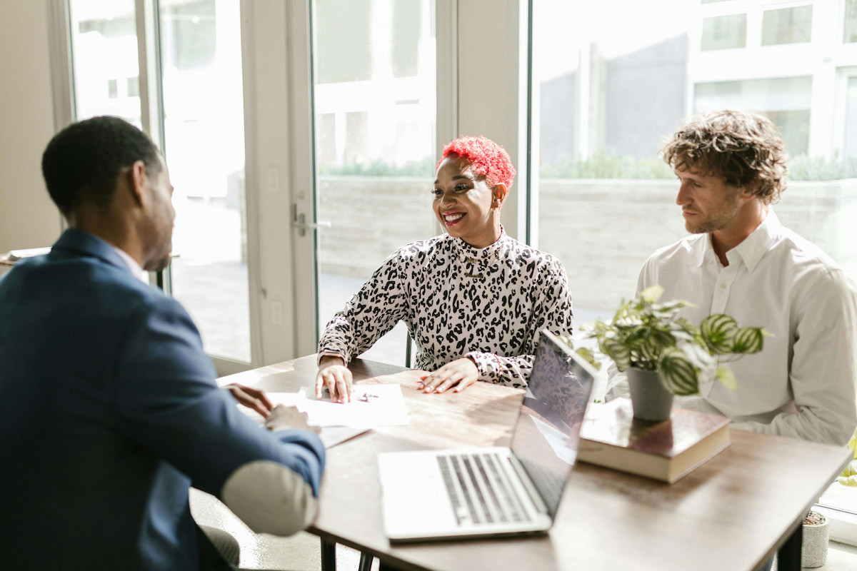 3 people at a table with laptop, smiling woman with pink hair